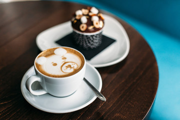 Cup of hot bear latte art coffee with delicious cupcake