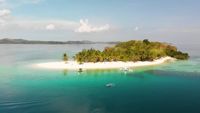 Aerial drone shot following a Paraw boat, in turquoise sea, around a beautiful, tropical isle, at Pass island, in Philippines, Asia