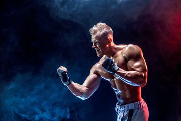 Fototapeta na wymiar Studio portrait of fighting muscular man in smoke on dark background