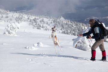 happy man playing with his dog in fresh snow in the mountains on a beautiful winter day