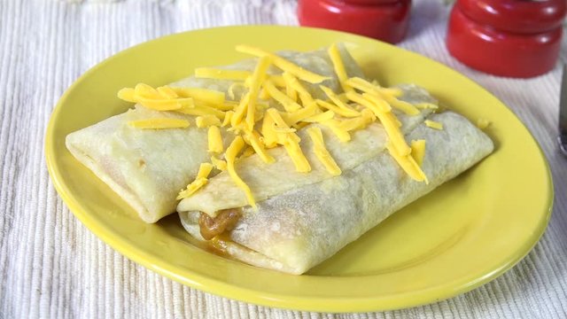 Sprinkling cheddar cheese on fresh cooked burritos slow motion
