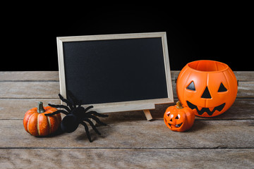 The chalkboard on the stand with Halloween Pumpkins, Black spider on wooden floor and black background