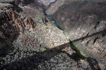 The bridge over the Rio Grande Gorge casts a long shadow across its 800' deep canyon, which lies on the Taos Plateau in New Mexico; view looking north from US Hwy 64