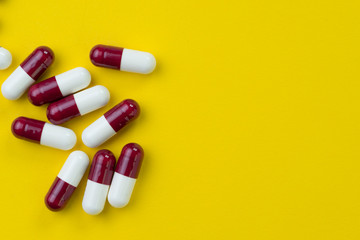 Medical, pharmacy or health care, drug and science concept, dark red and white capsules pills on yellow background with copy space