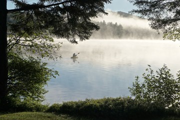 Obraz na płótnie Canvas Adirondack Park, New York, USA: A kayaker paddles across Sagamore Lake as morning mist rises from the water.