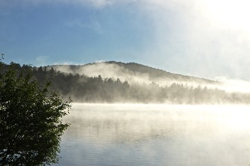 Fototapeta na wymiar Adirondack Park, New York, USA: The morning mist rises from the waters of Sagamore Lake.