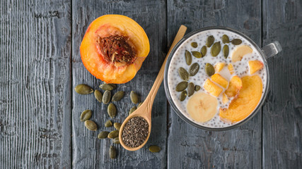 Chia seed pudding with peach and pumpkin seed on a dark wooden table. The view from the top. Flat lay.
