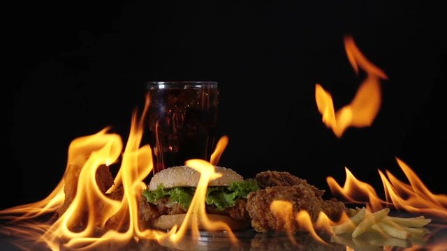 Hamburger and chicken fast food on fire slow motion background.