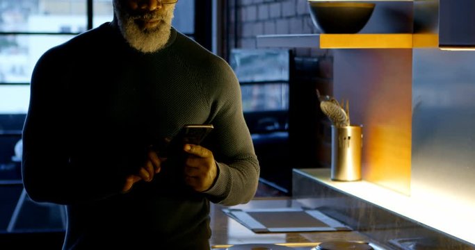 Senior man using mobile phone in kitchen 4k
