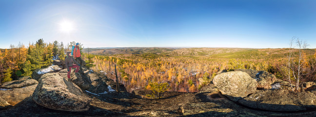 Couple of tourists with backpacks man and woman standing on a rock in autumn forest. Cylindrical...