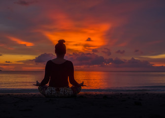 Silhouette of woman sit on the beach practice yoga at sunset