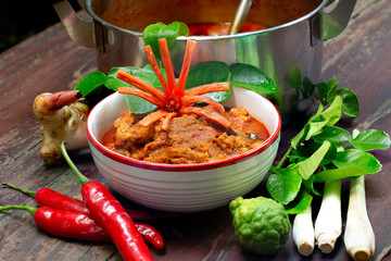 Chicken panang curry in the white bowl and fresh spice on old brown wooden background,