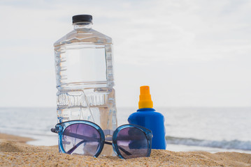 Sunglasses, Sunscreen and bottle of water on sand beach