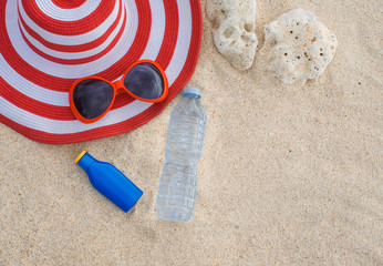Sunscreen, hat, sunglasses and bottle of water on sand beach