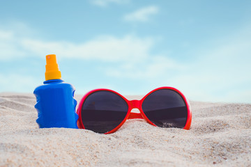 Sunscreen or sunblock lotion bottle with sunglasses on the beach. Summer concept