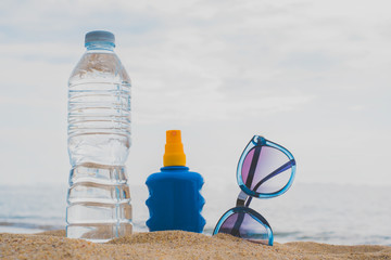 Sunglasses, Sunscreen and bottle of water on sand beach