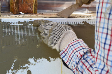 Worker hands in gloves installing fiberglass reinforcing mesh profile on  rigid polyurethane foam sheets wall around window sill. DIY home improvement and insulation process concept.
