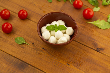 Italian food ingredients – mozzarella, tomatoes, arugula on rustic wooden table.