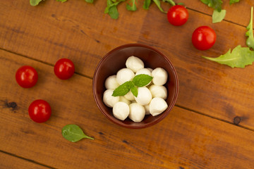 Italian food ingredients – mozzarella, tomatoes, arugula on rustic wooden table.