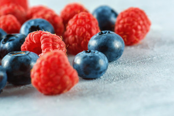 Blueberries and raspberries mix on the background of gray cement. Ripe and juicy fresh raspberries and blueberries close-up. A lot of berries close-up.