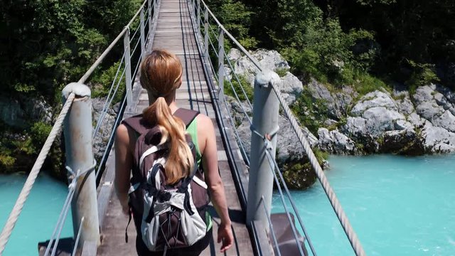 Young woman walking across the wooden bridge above Soča river