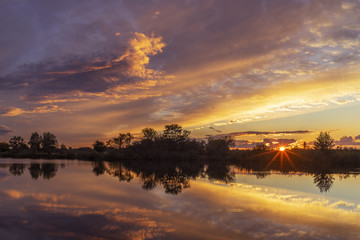 Obraz premium Magical sunset over the river in rural terrain. Natural calm beautiful landscape. The sun's rays.