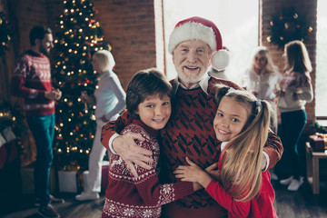 Portrait of cheerful grandpa in headwear hugging grandchildren. 