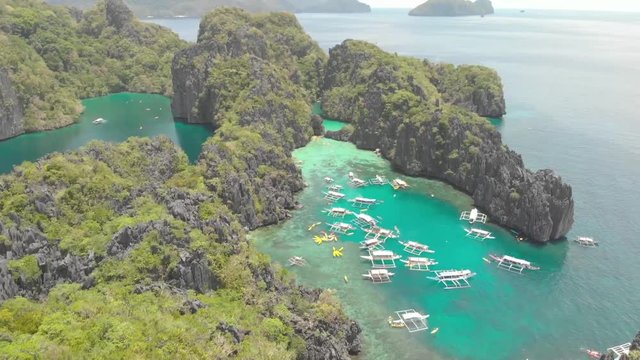 Aerial drone shot backwards over a turquoise lagoon and Paraw boats, between limestone cliffs on a sunny day, on Palawan island, in Philippine archipelago, Philippines, Asia