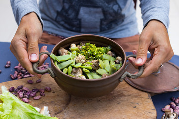 Woman hands hold a copper pot with cooked green beans, broccoli and mushrooms vegetables. Vegan vegetarian healthy food. Lunch or dinner.