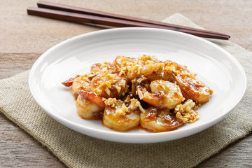 stir fried shrimp with garlic and spicy sweet sauce in a ceramic dish on wooden table. asian homemade style food concept.