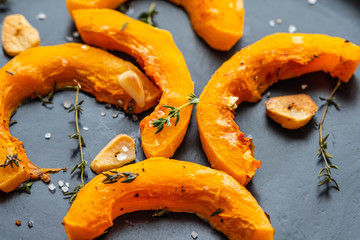 Cooked pumpkin pieces with garlic and rosemary on a black plate. Copy spase.