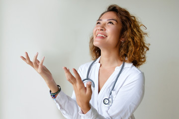 Happy Asian doctor praying for thank god. Young Asian woman in white coat with stethoscope raising...