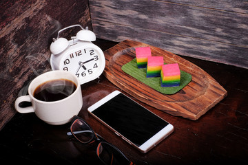 Traditional Malaysian food. Kuih Lapis , alarm clock and  a cup of coffee on wooden background....