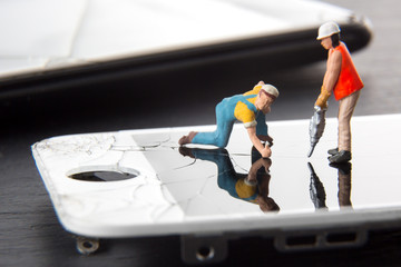 Mobile phone repair service concept. Miniature technician people repairing a cracked smart phone...