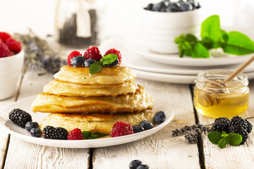 Pancakes with forest fruits berries on white table.