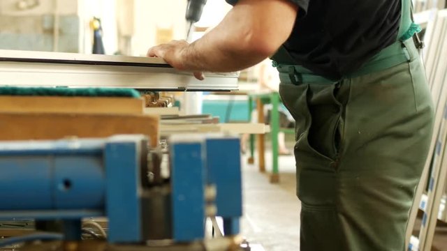 Production and manufacturing of pvc windows, a male worker assembles a pvc profile window, drills a hole in the pvc profile for mounting hinged parts, drill pvc window