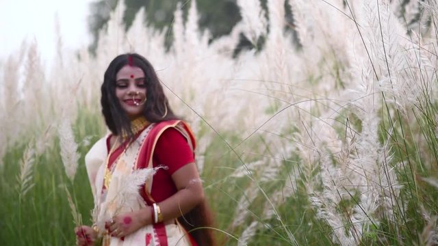 A playful and innocent Indian bengali woman wearing saree plays with the long white grass in a field or durga puja or poyla boisakh, Slow motion