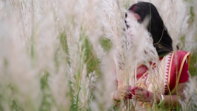 A happy and playful married Indian bengali woman wearing saree plays with the long white grass in a field for durga puja or poyla boisakh, Slow motion