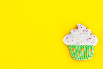 Colorful icing cookie in cupcake shape on yellow background