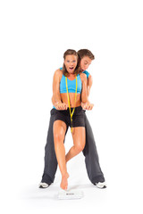 Caucasian man helping woman stand over weighing scale to check body weight with measuring tape wrapped around neck