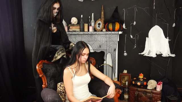 Young beautiful brunette reader dying as creepy violent woman in Death Reaper Halloween cape costume choking killing her