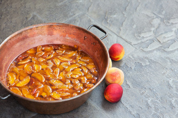 Fresh bright peaches and nectarins lay on the stone bricks, close to the copper jar, full of peach jam. Close up, outdoor, copy space.