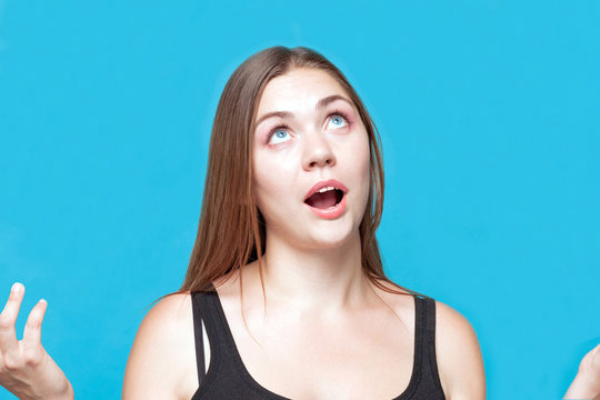 Attractive young caucasian woman with dark hair poses praying, hahds and blue eyes up, mouth open. Astonishment emotions. Studio, model, solated, copy space..