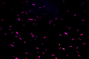 A few purple confetti fired on air during a festival at night. Image ideal for backgrounds. Black sky as background. Confetti illuminated by lights