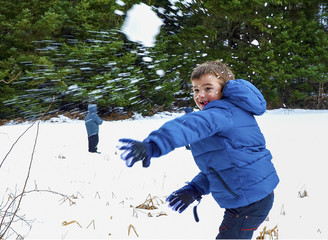Boy in blue warm coat having fun in beautiful winter place with snowballs