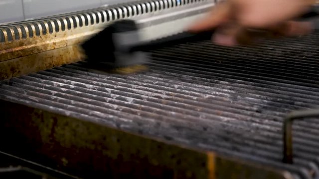 Cleaning a BBG grill in modern restaurant kitchen. Close up 4K footage