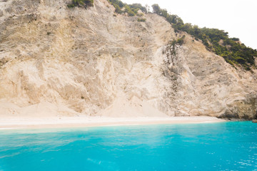 White beach, blue ocean and green rocks