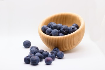 Beautiful blueberries spilled out of wooden bowl isolated on white background