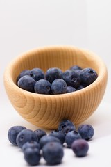 Handful of fresh blueberries partially spilled out of wooden bowl. Vertical, isolated on white