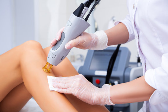 Close-up of a female cosmetologist in a medical coat making a young woman  a procedure laser hair removal for leg. Cosmetology, ionization, diamond procedures.